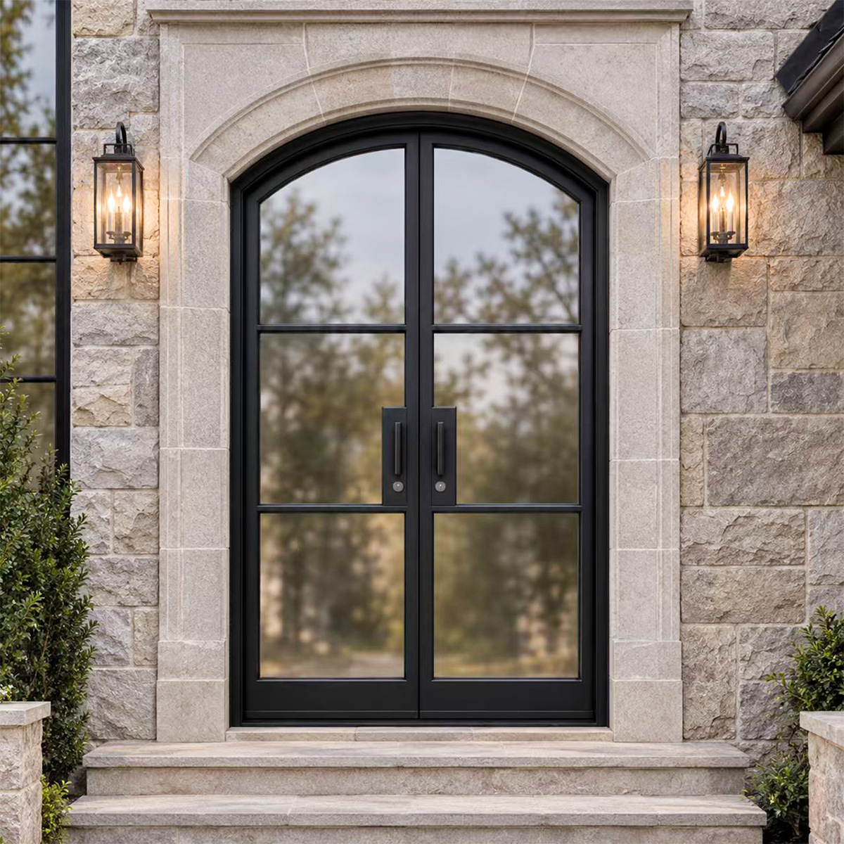 Arched double iron French entry doors with wide glass panels installed at an elegant stone home entrance