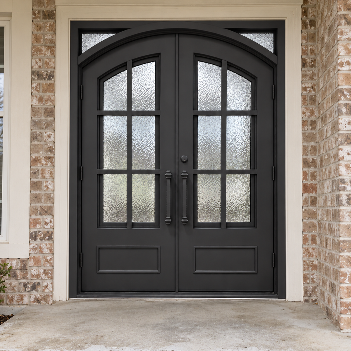 Black double modern iron doors with an eyebrow arch, divided textured glass, and solid lower panels in a brick entrance